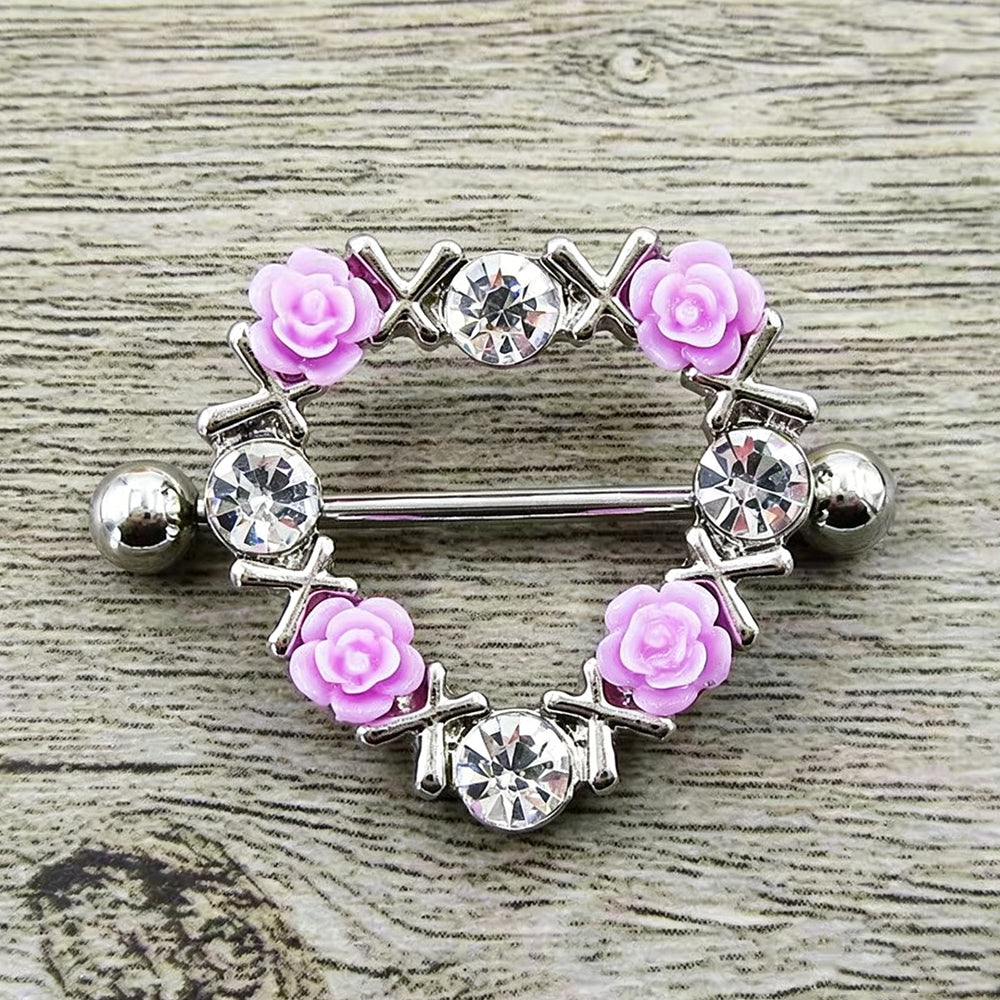Close-up shot of a silver heart-shaped alternative nipple piercing jewelry with pink flowers resting on a rustic grey wooden textured surface.