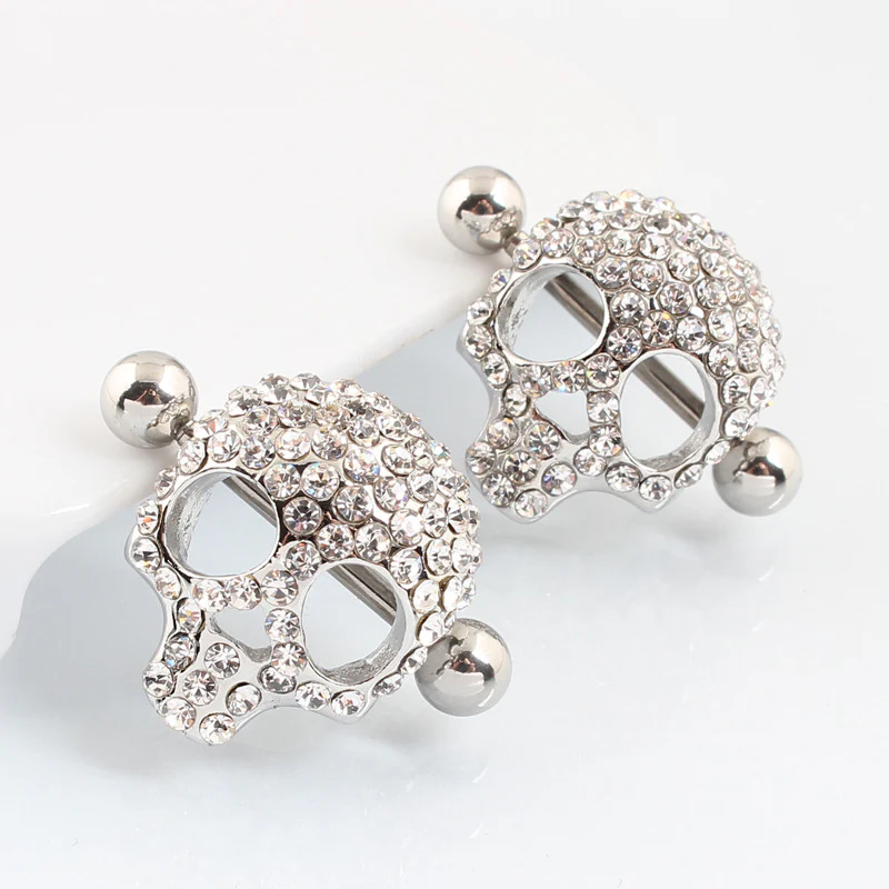 A pair of silver skull nipple shields with sparkling crystal pave, shown from a side angle.