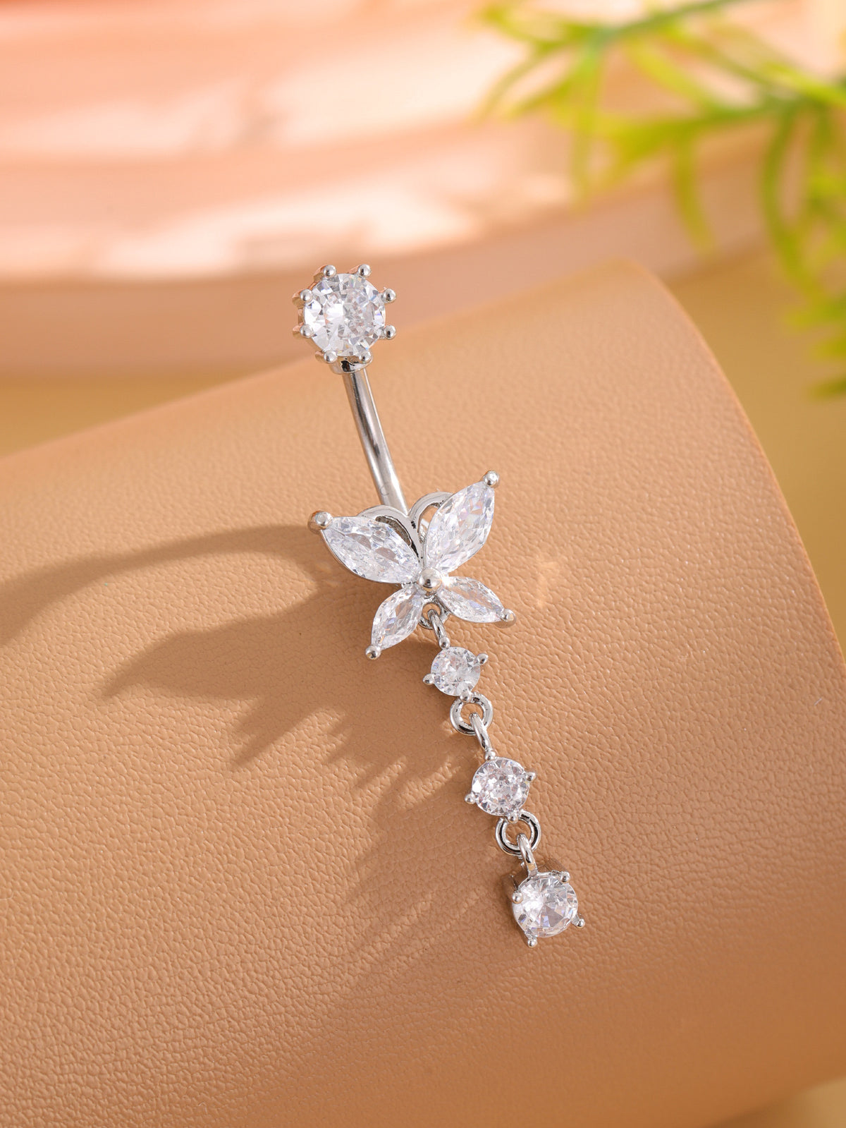 Single silver-tone butterfly cubic zirconia navel ring angled on tan display