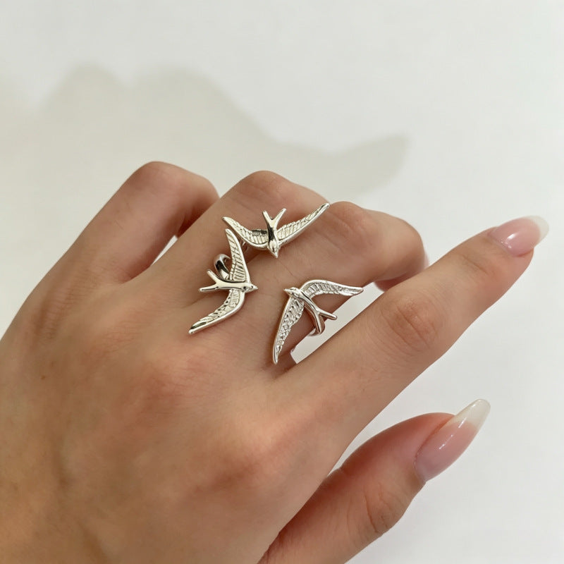 One silver-tone three-swallow ring on a bent hand, showing the birds from an angled view.