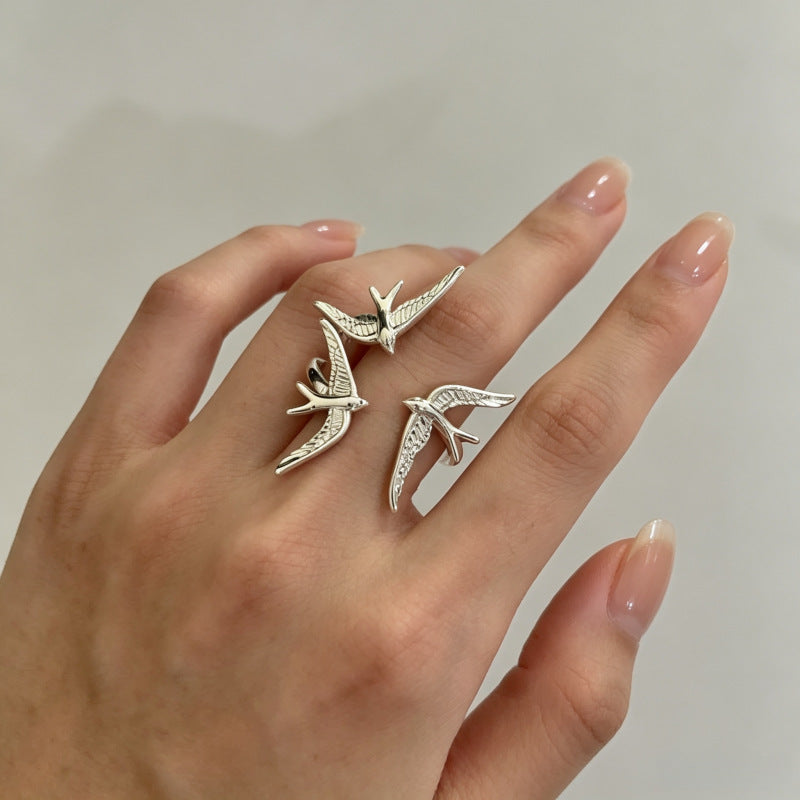 One silver-tone ring with three sculpted flying swallows worn on a hand.