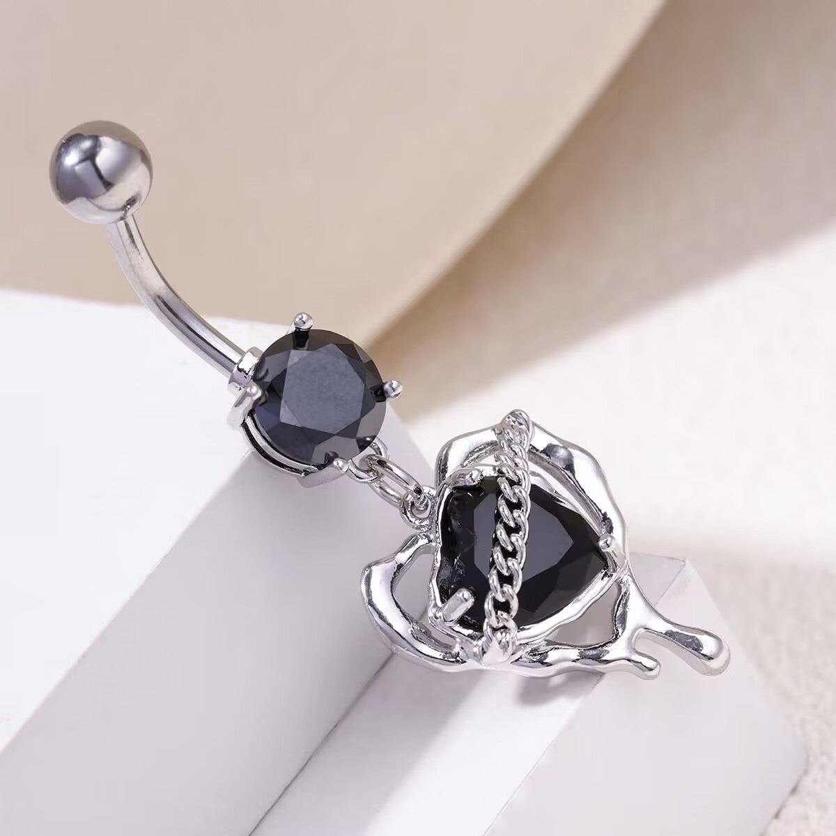 Close up of silver Y2K gothic style navel ring with molten lava heart frame and black gem