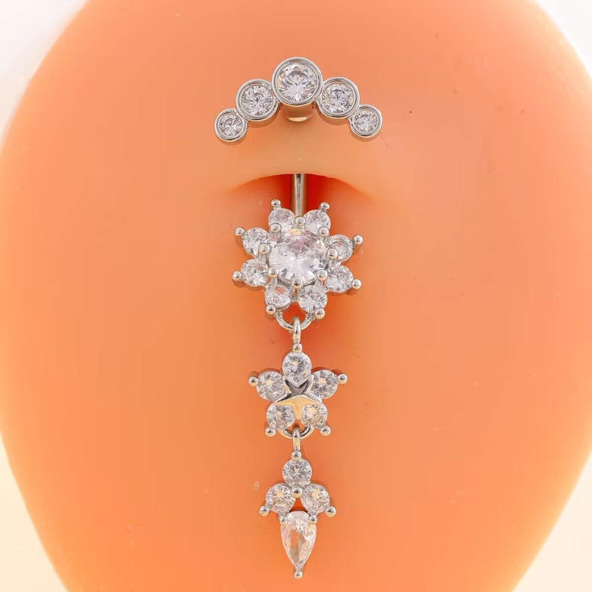 Silver zircon flower dangle belly button ring shown on model featuring curved barbell and teardrop CZ pendant.