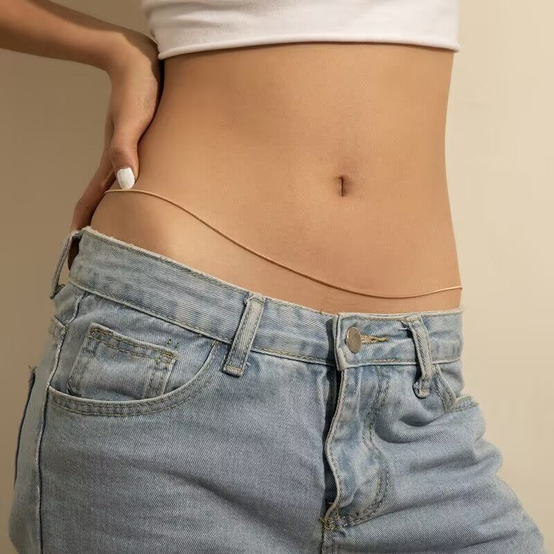 Single-strand minimalist gold belly chain styled casually with blue denim jeans.