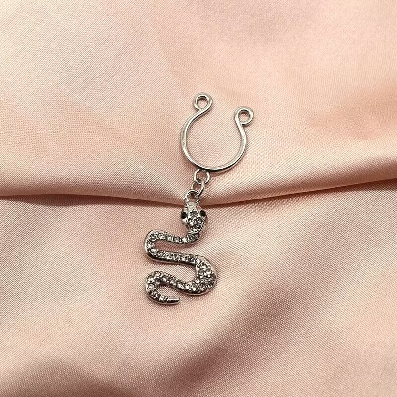 A silver snake-shaped non-pierced nipple ring with crystals lying on a soft pink silk background.