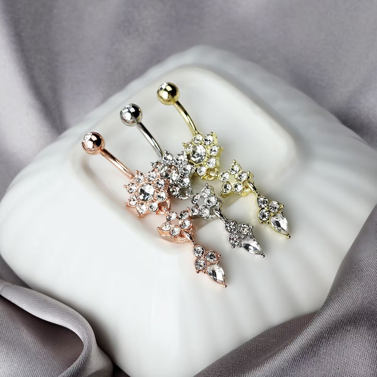 Elegantly displayed silver, gold, and rose gold dangle navel piercing jewelry with sparkling cubic zirconia accents.