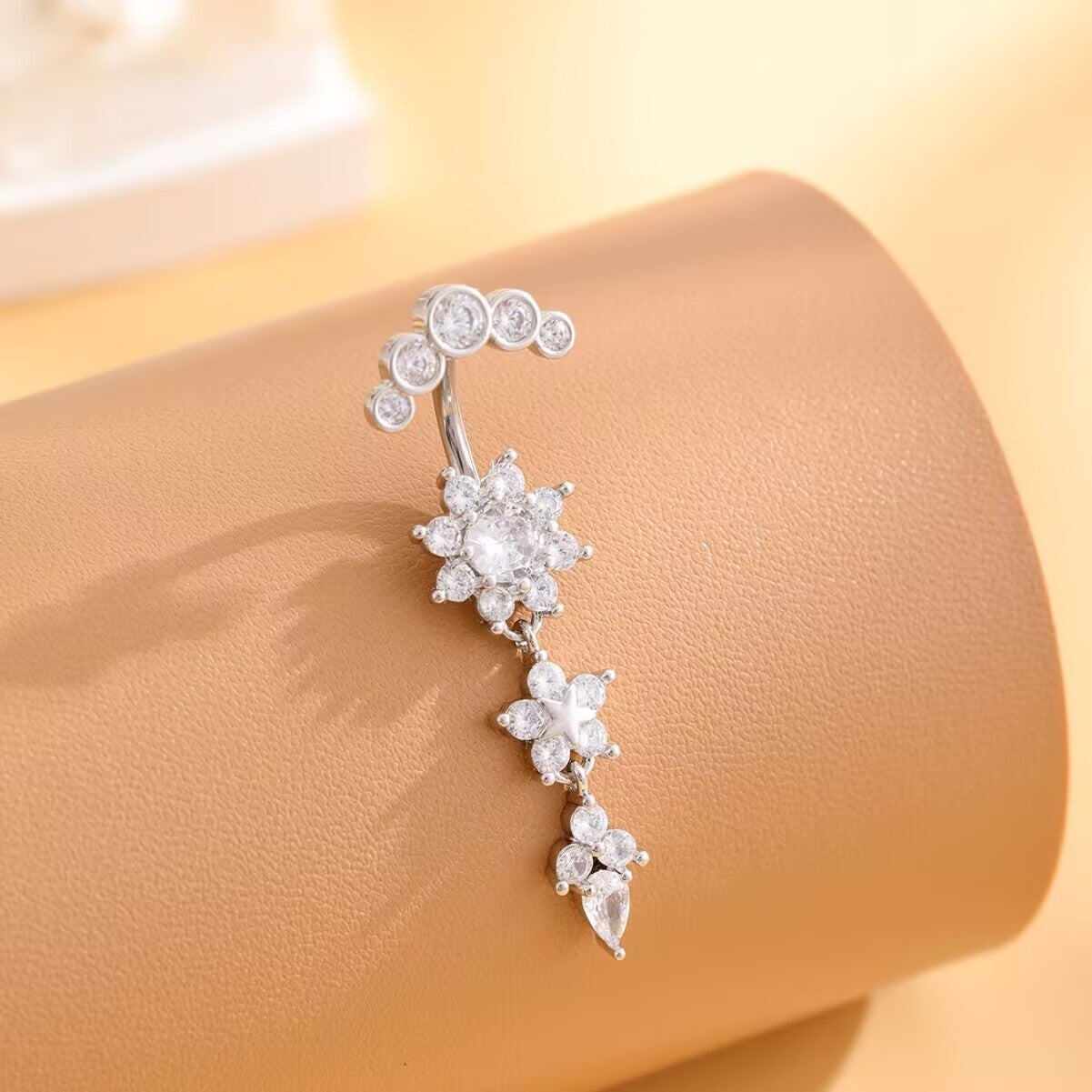 Sparkling silver CZ flower navel piercing jewelry displayed on display prop highlighting cubic zirconia shine.