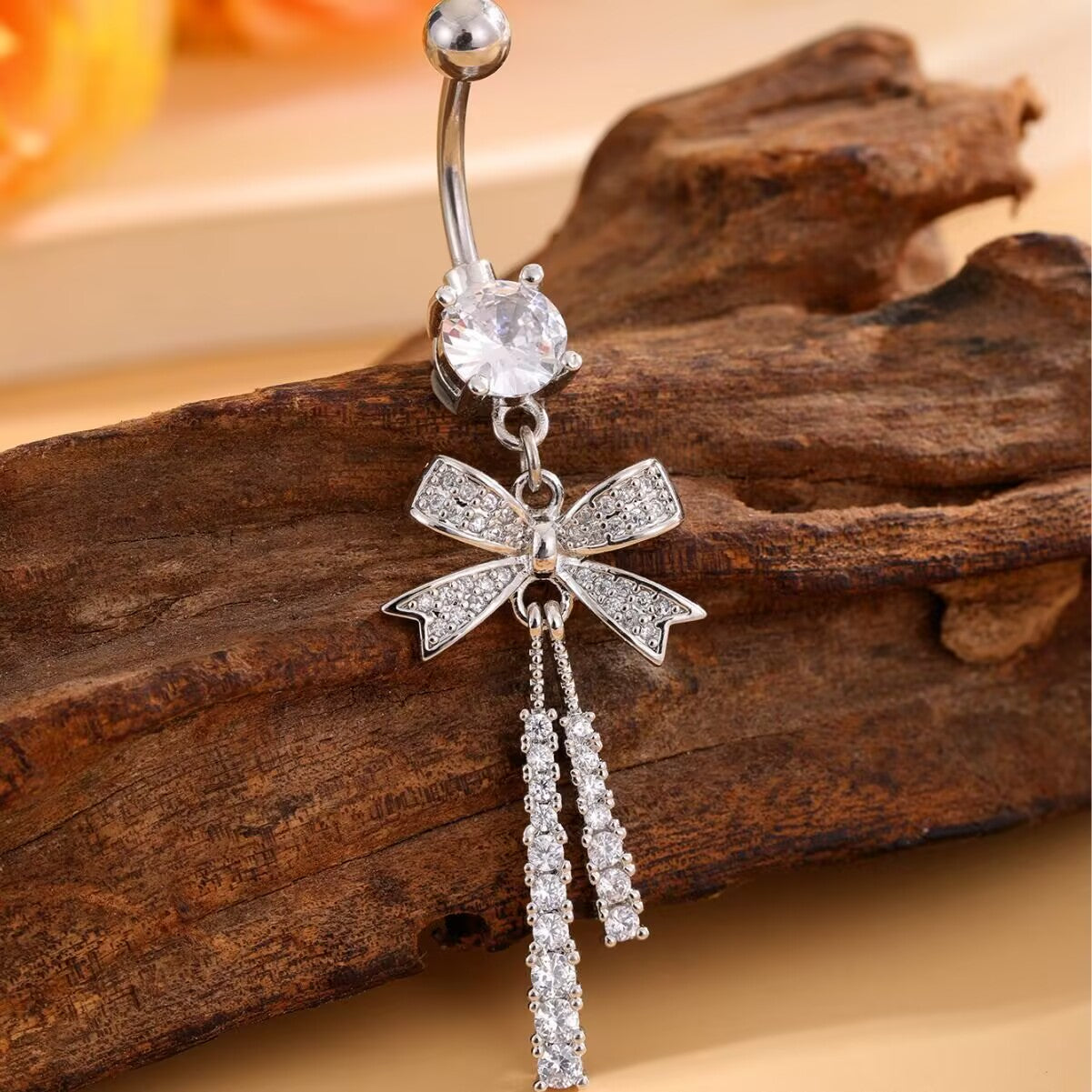 Close-up of a sparkling bowknot navel ring with long cubic zirconia tassels resting on a rustic wooden background