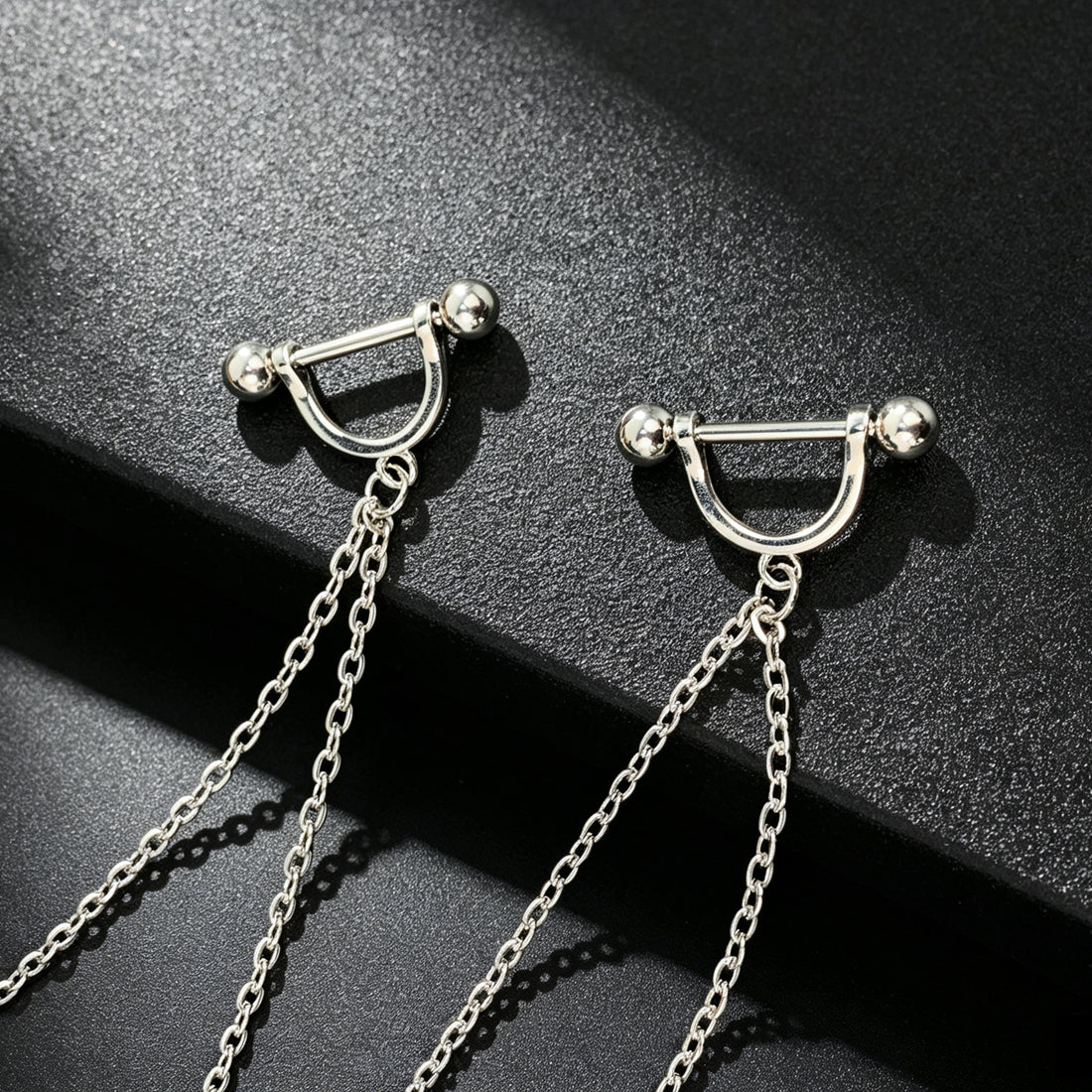 Close-up of dual-ball straight barbell nipple rings with U-shaped water-drop drapes connecting to body jewelry chains.