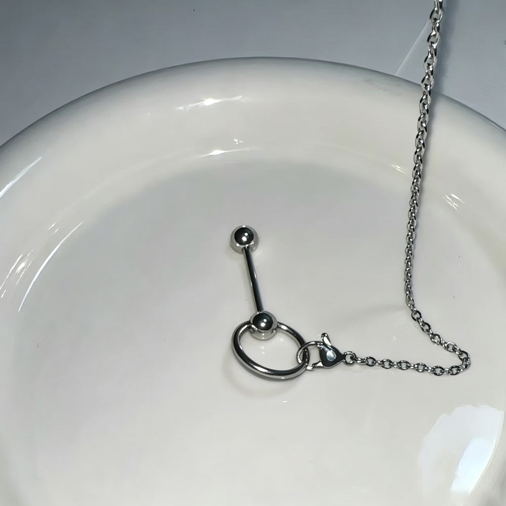Stainless steel 14G tongue ring barbell on a white ceramic plate, showing the chain’s lobster clasp secured to the barbell's slave ring.