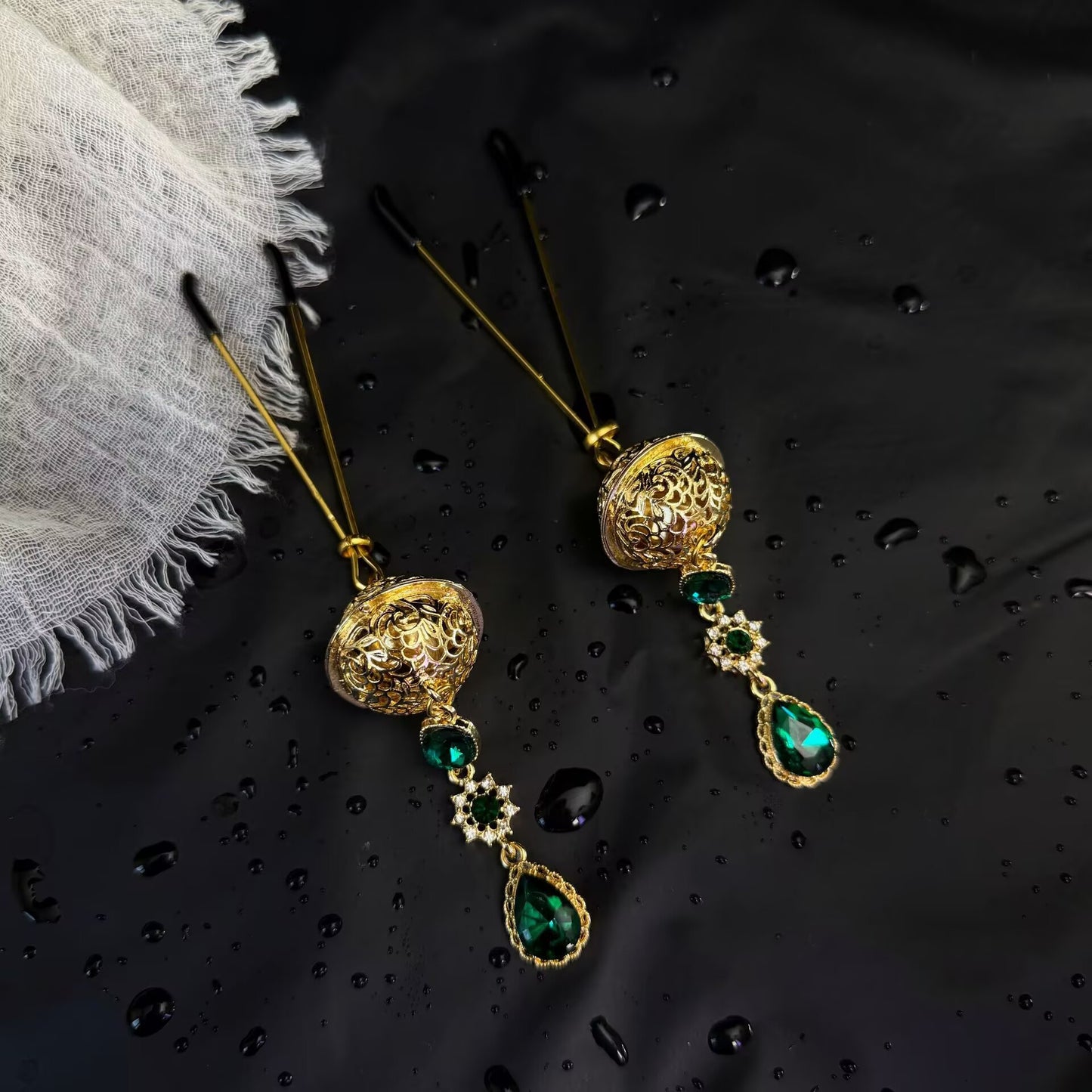 Angled view of U-bar pressure non-pierced nipple clamps featuring filigree ball design and teardrop emerald green stones.