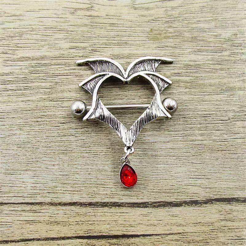 Real life product shot of the vintage grunge vampire heart nipple jewelry with a blood red teardrop gem resting on a rustic wooden surface.