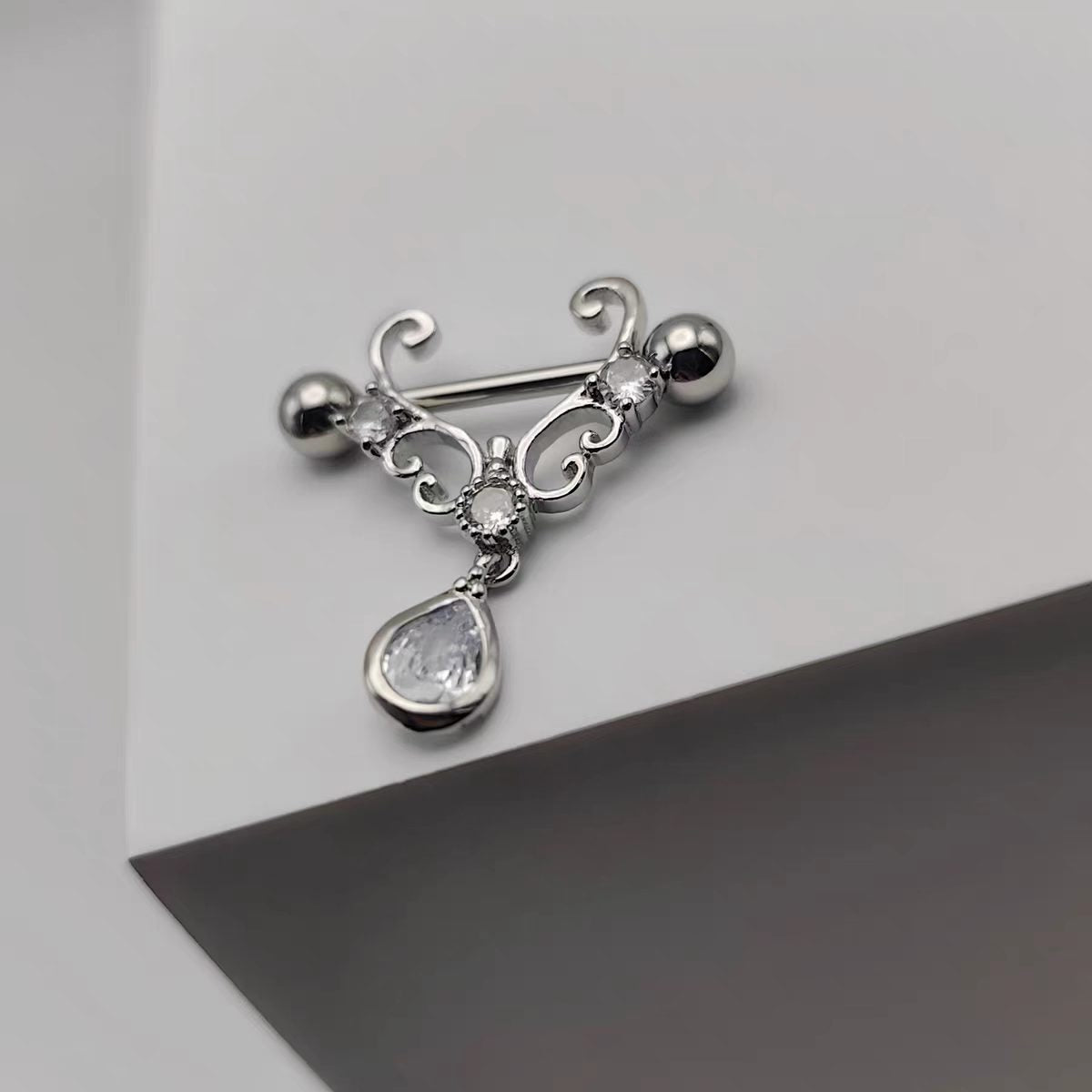 High-angle lifestyle shot of a crystal filigree nipple shield resting on a modern geometric surface.