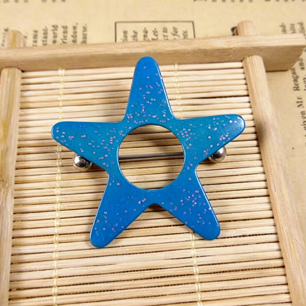 Real shot of a whimsigoth blue star nipple jewelry with fine pinkish glitter flakes, placed on a light wood bamboo tray with text backdrop.