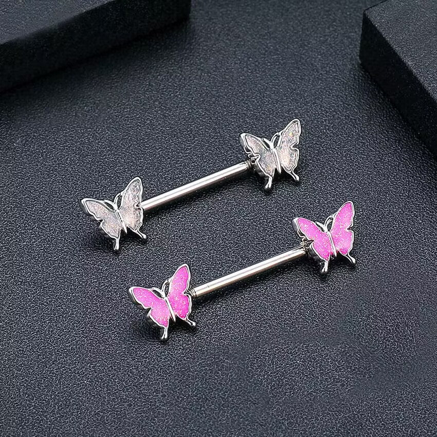 Close up shot of white glitter and pink glitter butterfly nipple barbells placed on a textured dark grey surface.