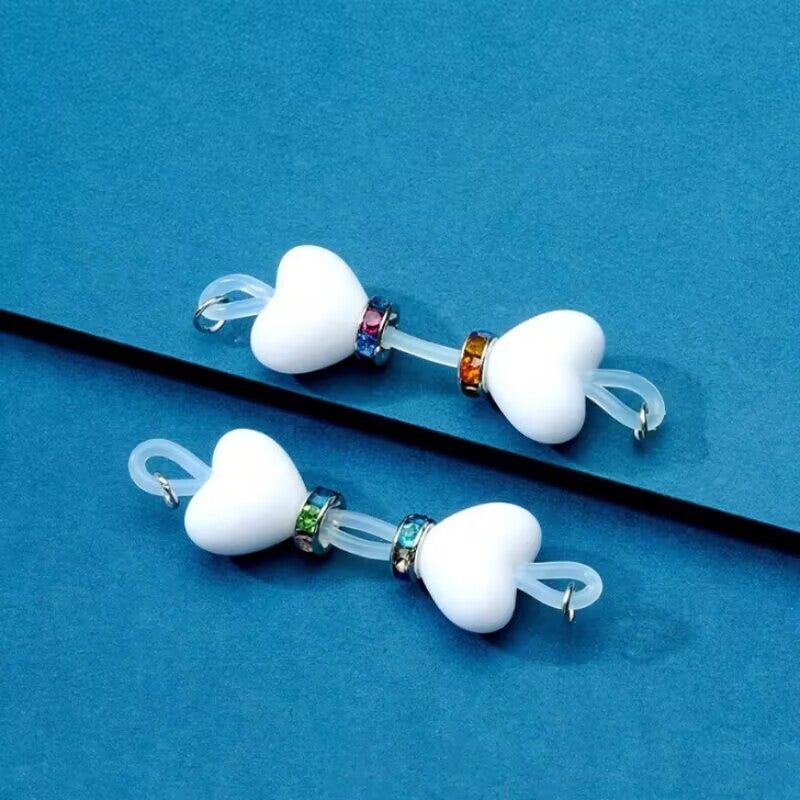 Pair of white heart non-piercing nipple jewelry with flexible clear silicone bands and rainbow rhinestone rings.