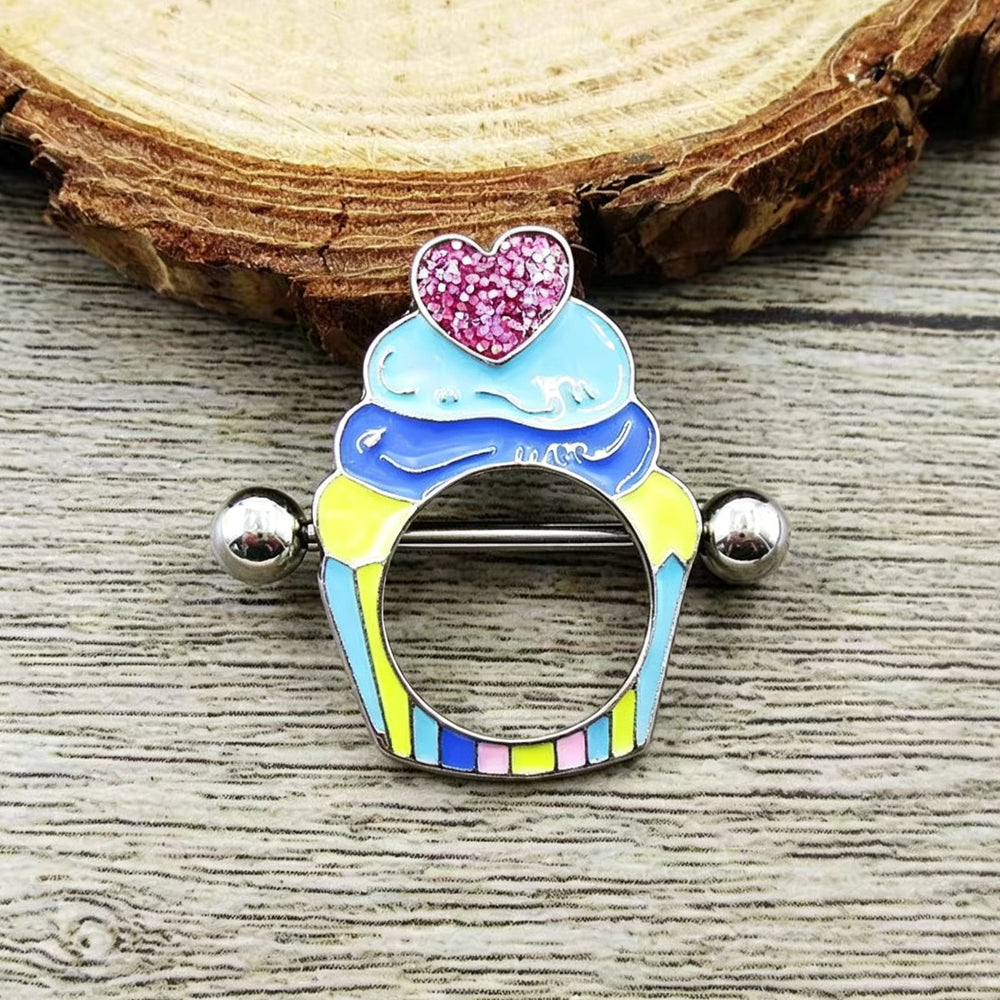 Real-life flat lay photo of a vintage Y2K aesthetic cupcake nipple piercing shield placed on a rustic wood slice background, displaying realistic texture and enamel colors.