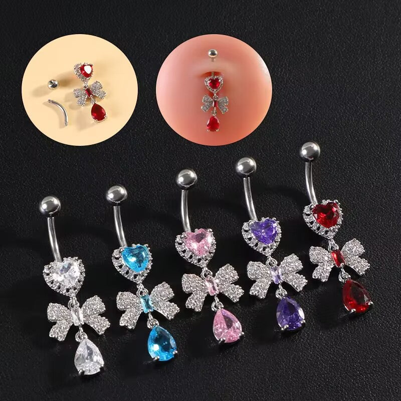A collection of romantic Y2K aesthetic dangling navel rings lined up on a black background displaying clear, blue, pink, purple, and red crystals.
