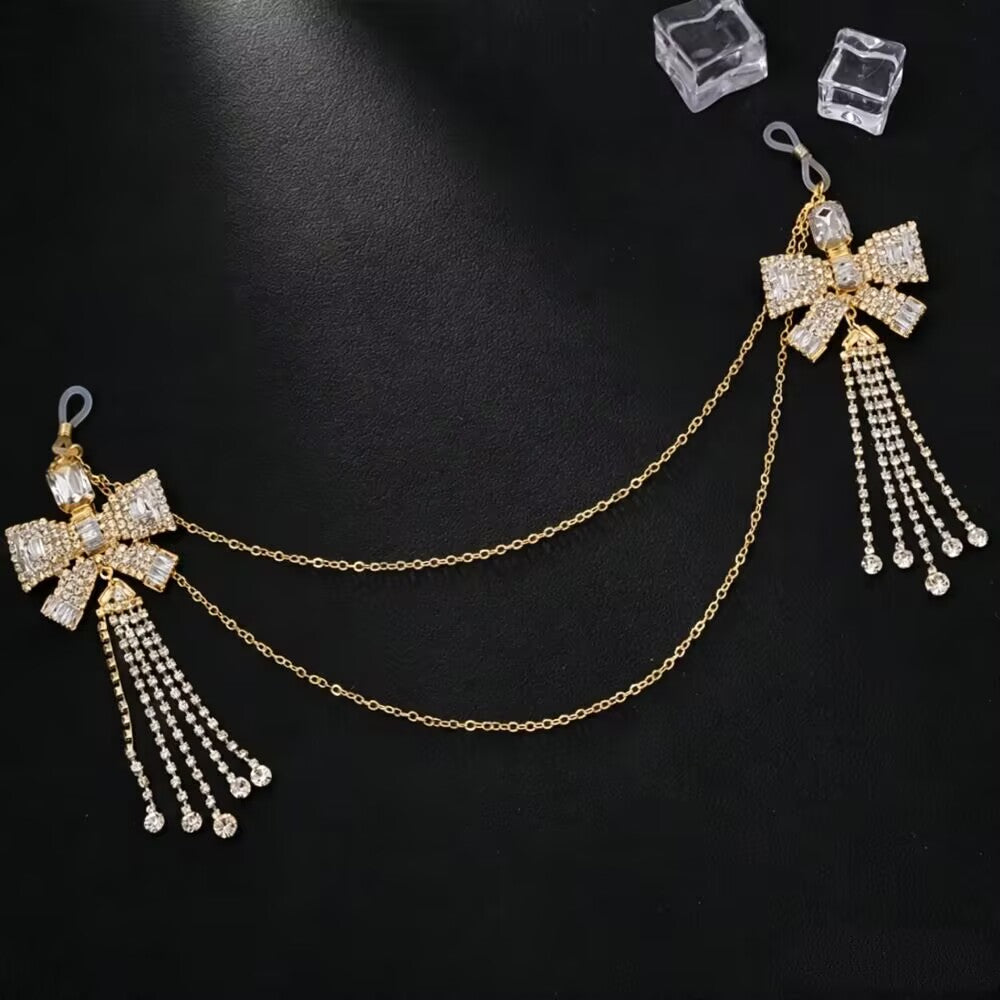 A gold Y2K crystal bowknot non piercing nipple chain body jewelry piece with long rhinestone fringe tassels flat lay on a black leather background.