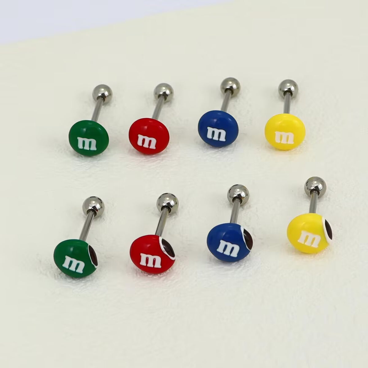 Eight M&M's chocolate candy tongue rings arranged in two rows showing red, blue, green, and yellow variants.