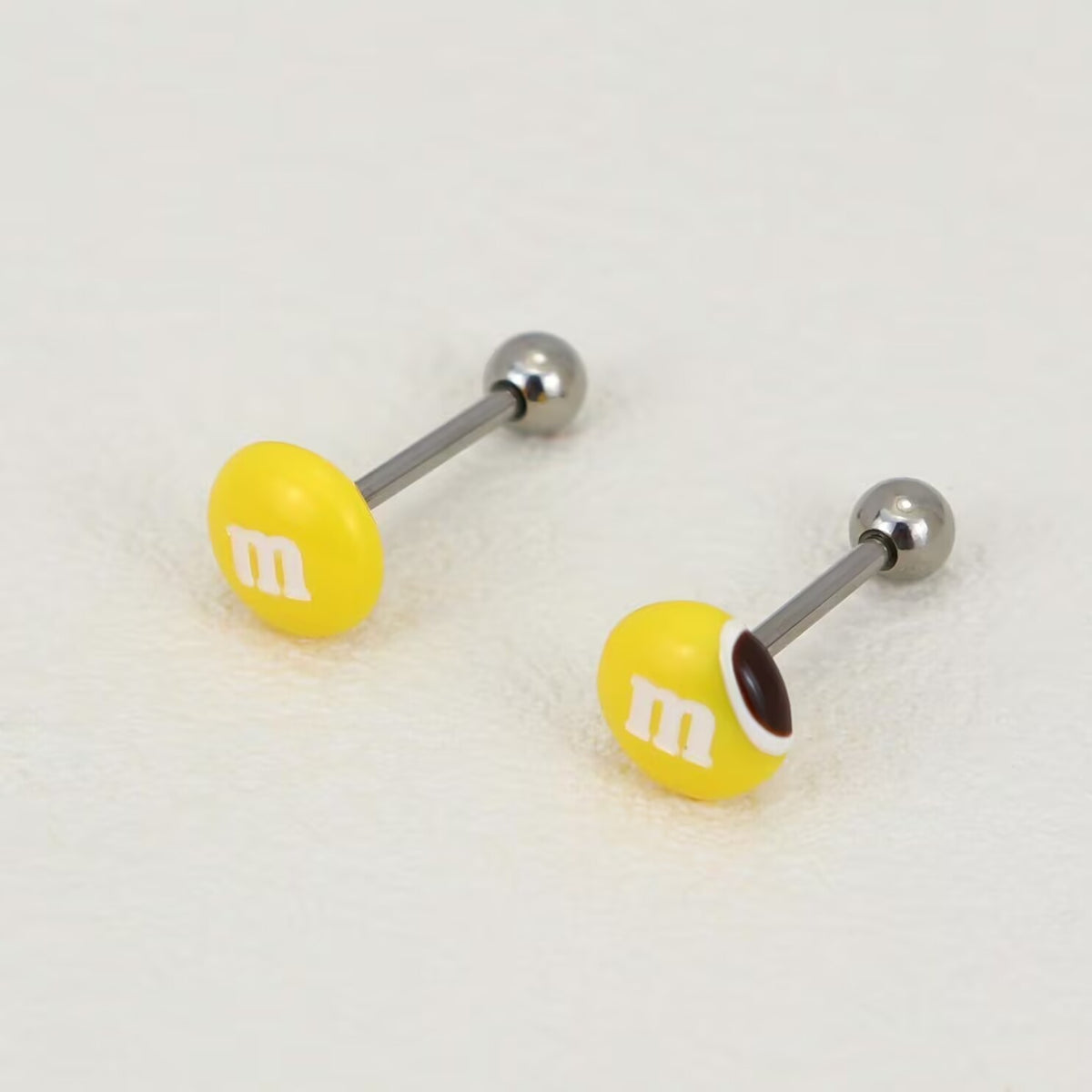Pair of yellow M&M's tongue barbells featuring one solid candy top and one bite-mark design.